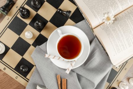 Red tea in white cup on top of chess board with book on side 